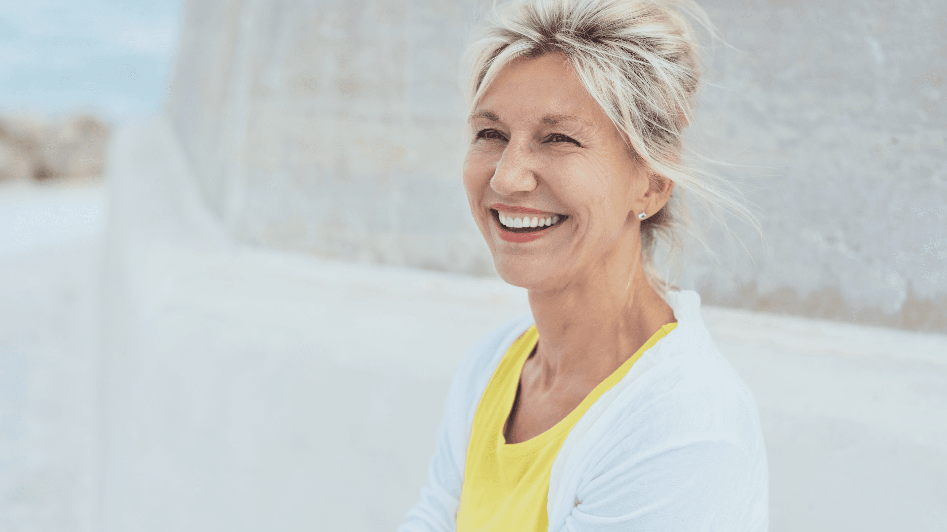 A woman in her fifties smiling, outdoors in bright light.